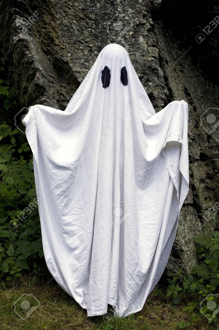 66477210-a-spooky-white-ghost-covered-by-a-sheet-with-slits-over-the-eyes-standing-in-front-of-a-rock-.jpg